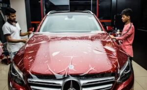 Two men install paint protection film on a maroon red Mercedes car